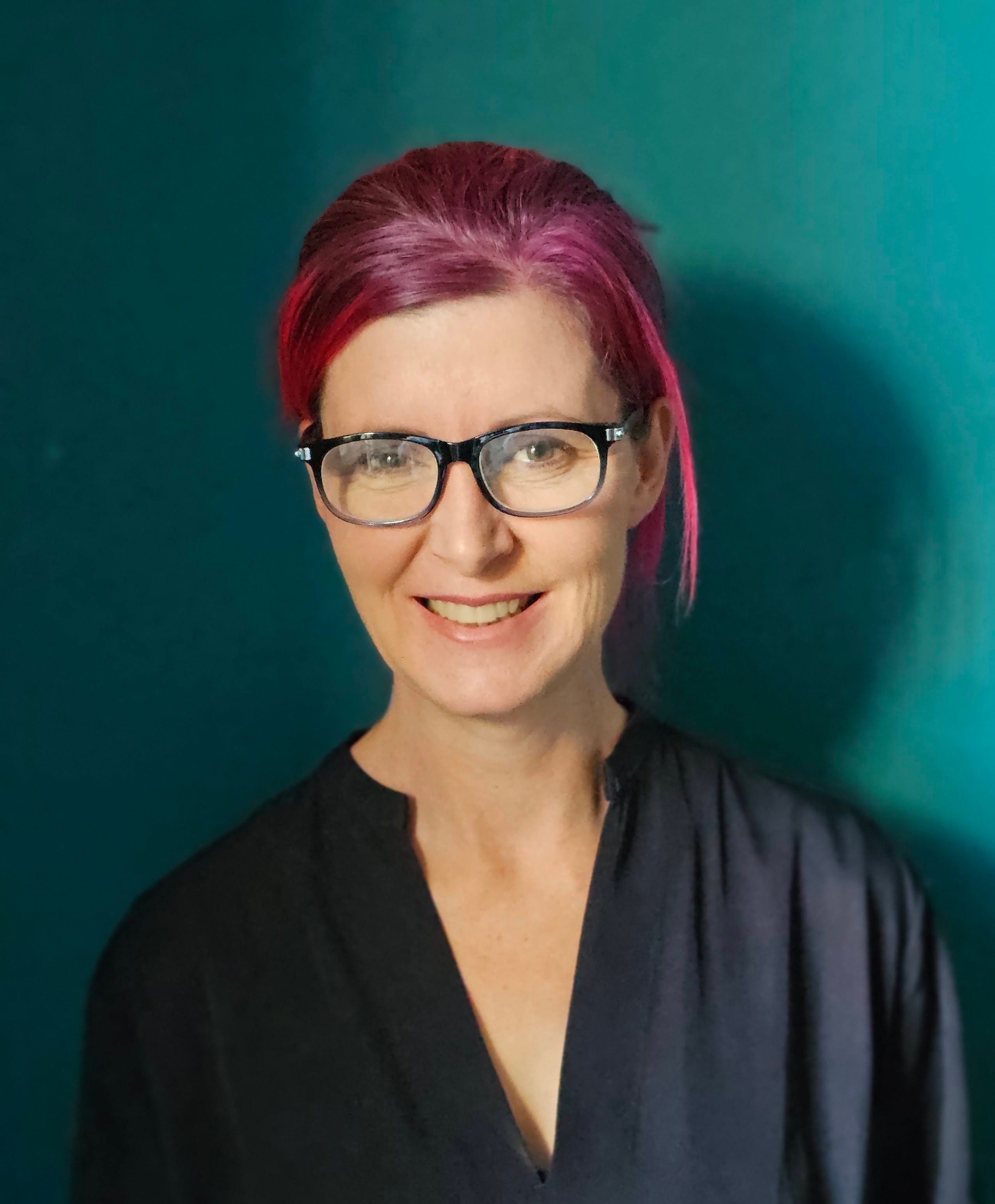 Portrait of Kate D’Anvers, relationship counsellor, smiling in front of a teal background.